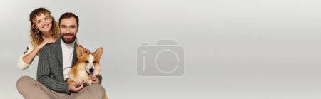 Photo for Family portrait, happy man and woman in winter attire posing with cute corgi on grey, banner - Royalty Free Image