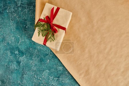 gift box with red ribbon and green juniper branch on wrapping paper and blue textures backdrop