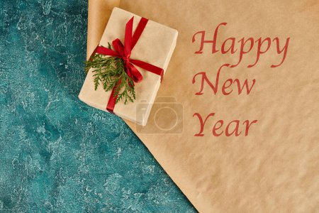 dekorierte Geschenkschachtel auf Bastelpapier mit frohem Neujahrsgruß auf blauer Oberfläche, Weihnachtsbasteleien