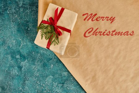 decorated gift box on craft paper with Merry Christmas inscription on blue textured backdrop