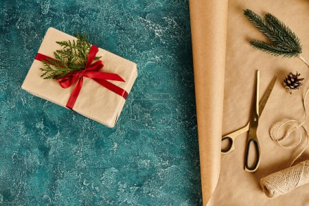 Caja de regalo de Navidad sobre fondo azul texturizado cerca de papel artesanal y tijeras con suministros de decoración