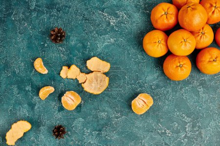 top view of juicy tangerines and pine cones on blue rustic surface, colorful Christmas background