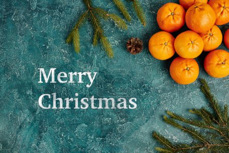 Merry Christmas greeting near mandarins and fir branches with pine cone on blue textured backdrop