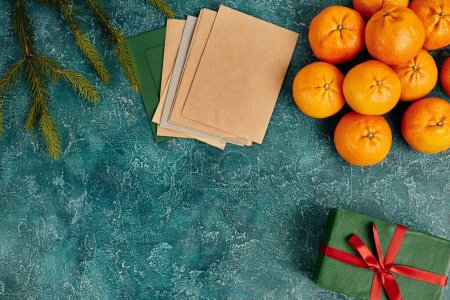 mandarinas frescas y sobres multicolores cerca de ramas de pino en textura azul, bodegón de Navidad