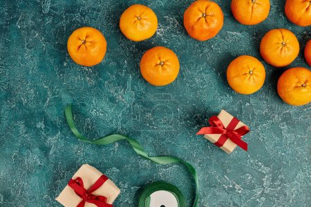 decorated gift boxes near fresh mandarins and ribbon on blue textured surface, Christmas still life