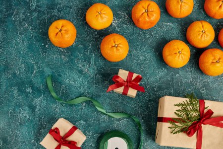 mandarinas maduras y cajas de regalo decoradas cerca de cinta en la superficie de textura azul, tema de Navidad