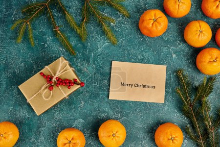sobre con letras de Feliz Navidad cerca de mandarinas y caja de regalo con bayas de acebo, Navidad