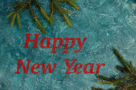 feliz año nuevo inscripción en la superficie de textura azul cerca de ramas de pino verde, fondo festivo