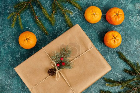 dekorierte Geschenkbox in der Nähe von reifen Mandarinen und Kiefernzweigen auf blau strukturiertem Hintergrund, Weihnachtsthema