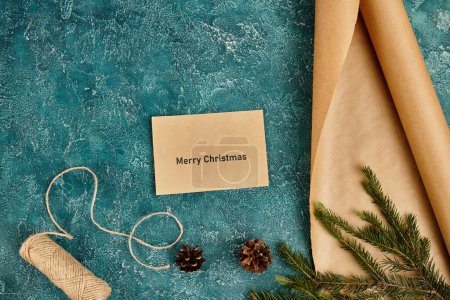 Téléchargez les photos : Enveloppe avec Joyeux Noël lettrage près de papier artisanal et ficelle sur la surface bleue avec décor de pin - en image libre de droit