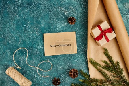 envelope with Merry Christmas greeting near pine decor and diy supplies on blue textured backdrop
