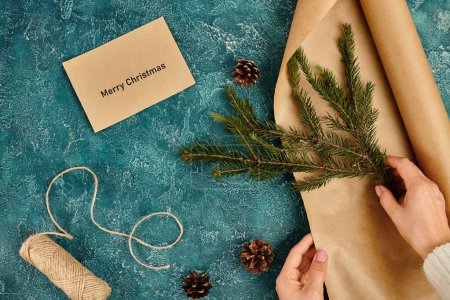 vista parcial de la mujer con rama de pino cerca de sobre con letras de Feliz Navidad y artículos de bricolaje
