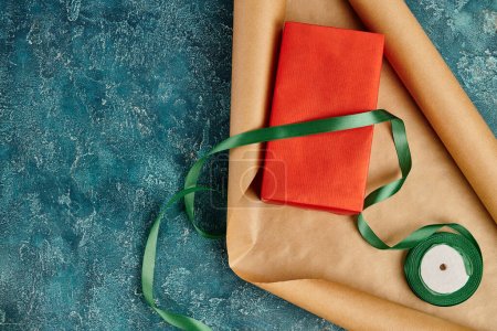 rote Geschenkschachtel und Bastelpapier mit dekorativem Band auf blau strukturiertem Hintergrund, diy Weihnachtsgeschenk
