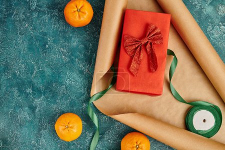 caja de regalo con cinta roja cerca de papel artesanal y mandarinas en la superficie de textura azul, tema de Navidad