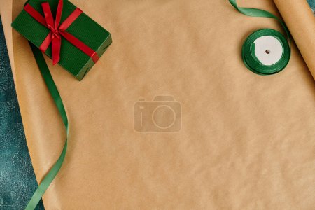 diy Christmas present, green gift box with red bow near decorative ribbon on craft wrapping paper