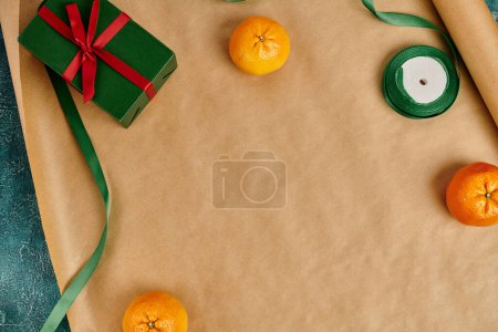 Draufsicht auf reife Mandarinen und grüne Geschenkschachtel mit roter Schleife und dekorativem Band auf Bastelpapier