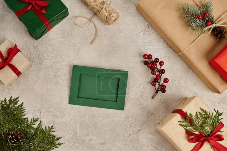 grüne Grußkarte und in der Nähe Geschenkboxen mit Tannenzweigen und Stechpalmen, weihnachtlicher Hintergrund