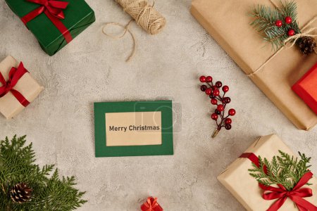 Merry Christmas greeting card near gift boxes and festive Christmas decor on grey textured surface