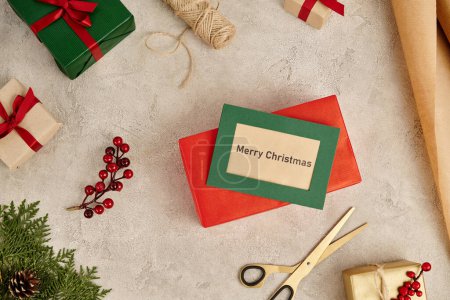 Frohe Weihnachten Grußkarte in der Nähe von bunten Geschenkboxen und Wacholderzweigen mit Stechpalmen