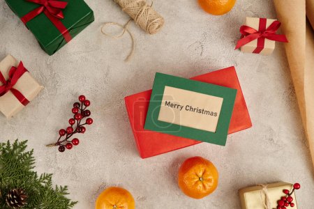 Merry Christmas greeting card near tangerines and decorated gift boxes on grey textured backdrop