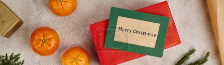 Mandarinen und Frohe Weihnachten Grußkarte in der Nähe von Geschenken auf strukturierter Oberfläche, horizontales Banner