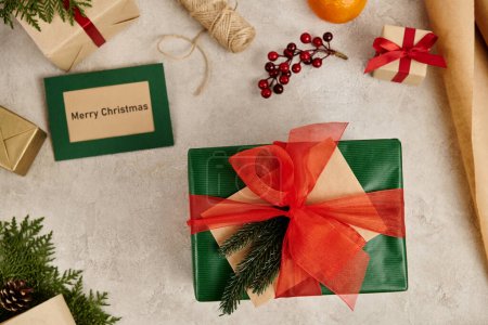 Téléchargez les photos : Boîte cadeau avec noeud en mousseline rouge près de Joyeux Noël carte de voeux et cadeaux avec décor festif - en image libre de droit