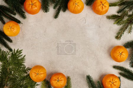 Marco de Navidad con mandarinas maduras cerca de enebro y ramas de pino sobre fondo texturizado gris