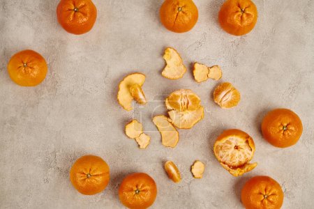 top view of whole and peeled juicy tangerines on grey textured backdrop, Christmas centerpiece