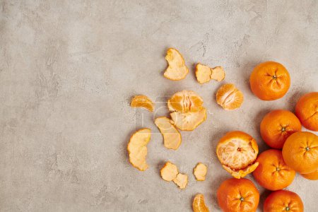 top view of whole and peeled ripe mandarins on grey textured backdrop, Christmas concept