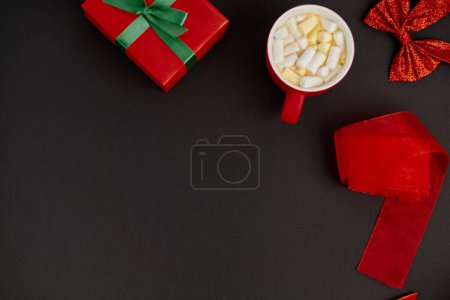 mug of hot chocolate with marshmallow near gift box and shiny bow with red ribbon on black backdrop