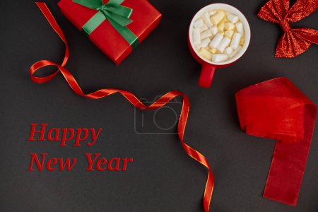 feliz año nuevo letras cerca de caja de regalo y lazo brillante con cinta en el fondo negro, vibraciones festivas