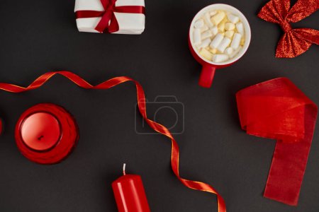 mug of hot chocolate with marshmallow near red ribbons and candles on black, Christmas backdrop