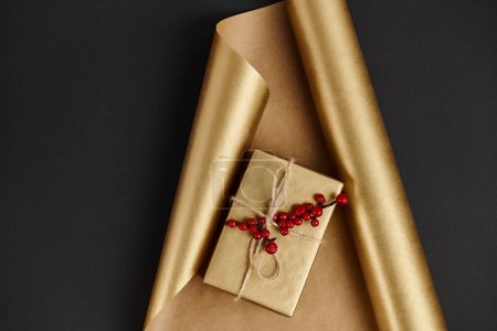 glänzende Geschenkschachtel mit roten Stechpalmen auf goldenem Geschenkpapier und schwarzem Hintergrund, Weihnachtsdekor