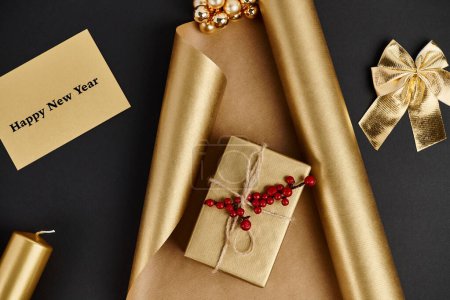 golden Christmas decor, new year greeting card near gift box and shiny wrapping paper on black