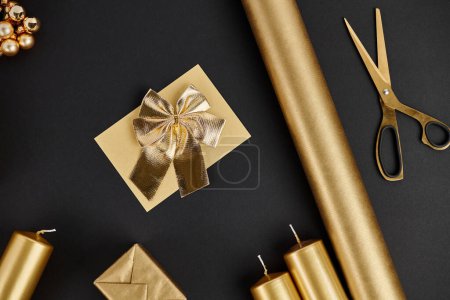 objets de Noël dorés sur fond noir, ciseaux près de papier roulé et bougies, artisanat de vacances