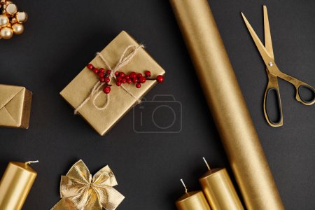 golden and shiny Christmas objects on black, scissors near rolled paper and candles, diy crafts