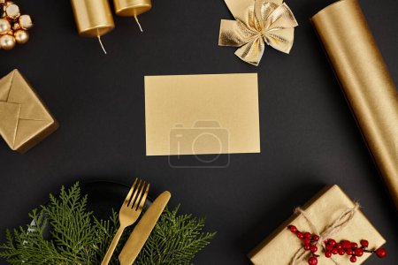 leere Grußkarte mit Kopierraum neben goldenem Besteck und glänzendem Weihnachtsdekor auf schwarz