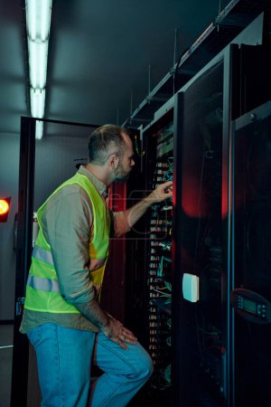 handsome technician with beard in safety vest inspecting data center attentively, maintenance