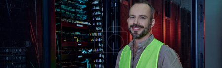 good looking jolly man in safety vest smiling at camera during inspection, data center, banner
