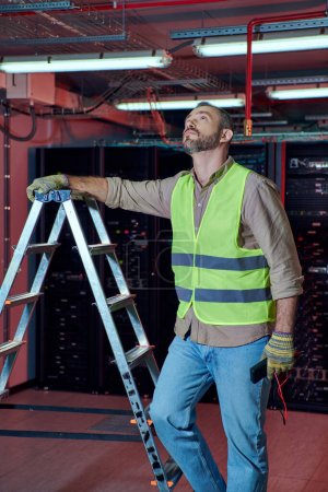 good looking hardworking technician standing next to step ladder and looking up in data center