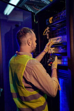 Photo for Good looking devoted technician in safety vest and gloves checking data center with detector - Royalty Free Image