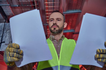 Photo for Good looking hardworking professional in safety clothes looking at his papers during inspection - Royalty Free Image