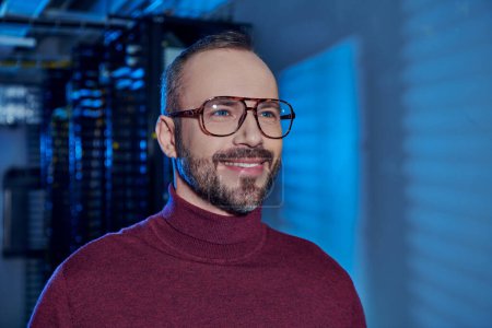 Photo for Cheerful good looking specialist in turtleneck with glasses smiling and looking away, data center - Royalty Free Image