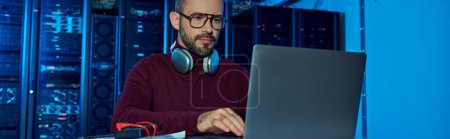 Photo for Focused joyful specialist in turtleneck with headphones working on his laptop, data center, banner - Royalty Free Image