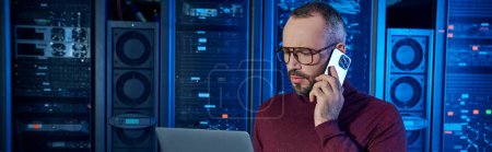 Photo for Devoted specialist in turtleneck talking by phone and looking at his laptop, data center, banner - Royalty Free Image