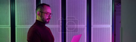 Téléchargez les photos : Joyeux professionnel à col roulé avec lunettes et barbe travaillant sur ordinateur portable, centre de données, bannière - en image libre de droit