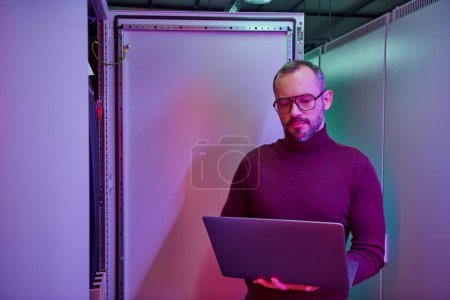 handsome hardworking data center specialist in turtleneck looking at his laptop attentively