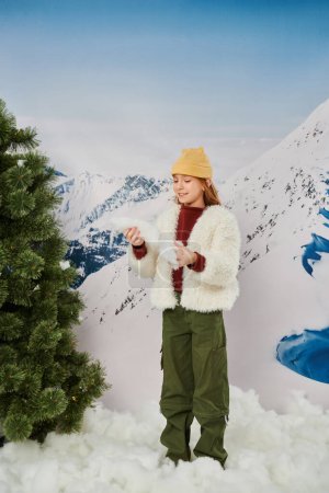 cheerful preteen girl in warm stylish outfit with beanie hat with mountain backdrop, fashion concept