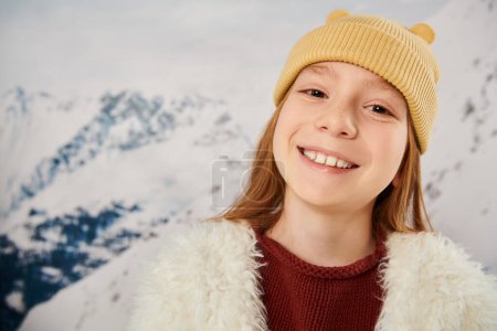 portrait of joyful little cute girl in beanie hat smiling cheerfully at camera, fashion concept