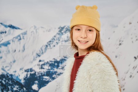 portrait of stylish little girl in warm trendy outfit smiling at camera with mountain backdrop